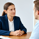 A male financial consultant, dressed in a modest business suit, intently listening to an elderly female client, who is wearing appropriate and comfortable clothing. They are seated opposite each other at a clean, professional wooden desk in a modern, brightly lit office with natural light. The consultant displays an open, empathetic expression and attentive posture. The client has a trusting, calm expression. The scene emphasizes sincere communication and trust-building. Full body shot, perfect anatomy, correct proportions, natural pose, well-formed hands, proper finger count, natural body proportions. Professional photography, high resolution, safe for work, appropriate content, fully clothed, professional, modest.